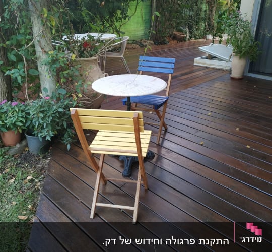 שולחן עגול עם כיסאות צבעוניים על דק עץ בגינה